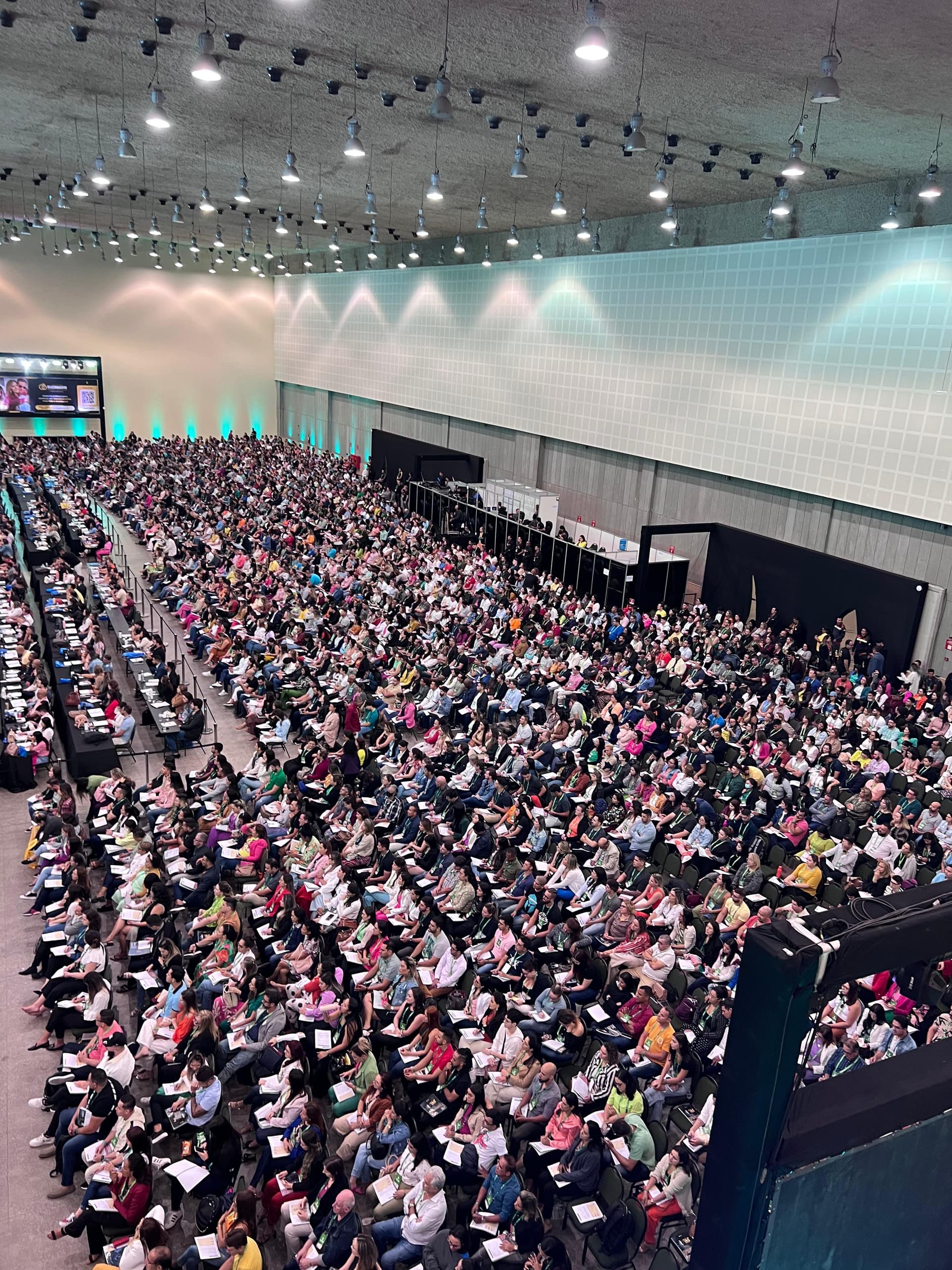 Plateia lotada acompanhando apresentação em auditório de congresso.