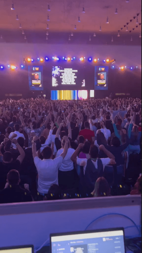 Público com os braços erguidos durante momento de energia no palco.