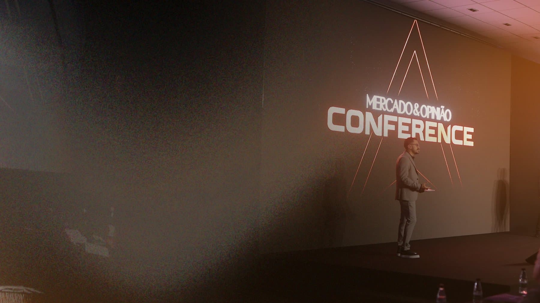 Palco do Mercado & Opinião Conference com projeção da marca ao fundo.